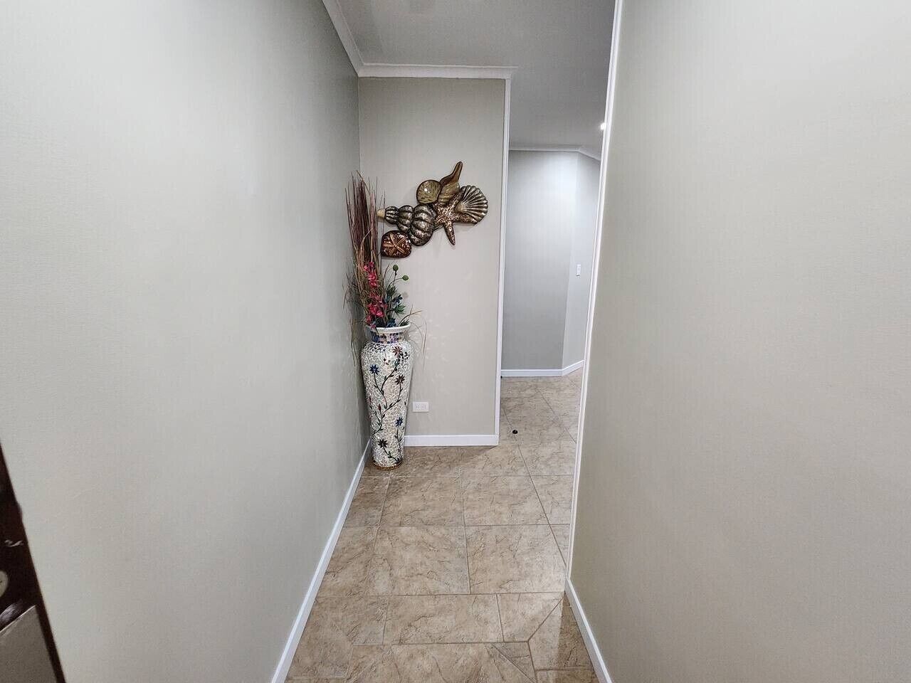 Un pasillo estrecho con un adorno de pared y un florero con flores.
