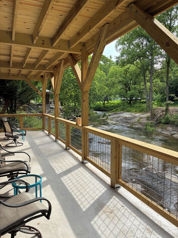 A covered outdoor seating area with chairs and a railing overlooking a river.