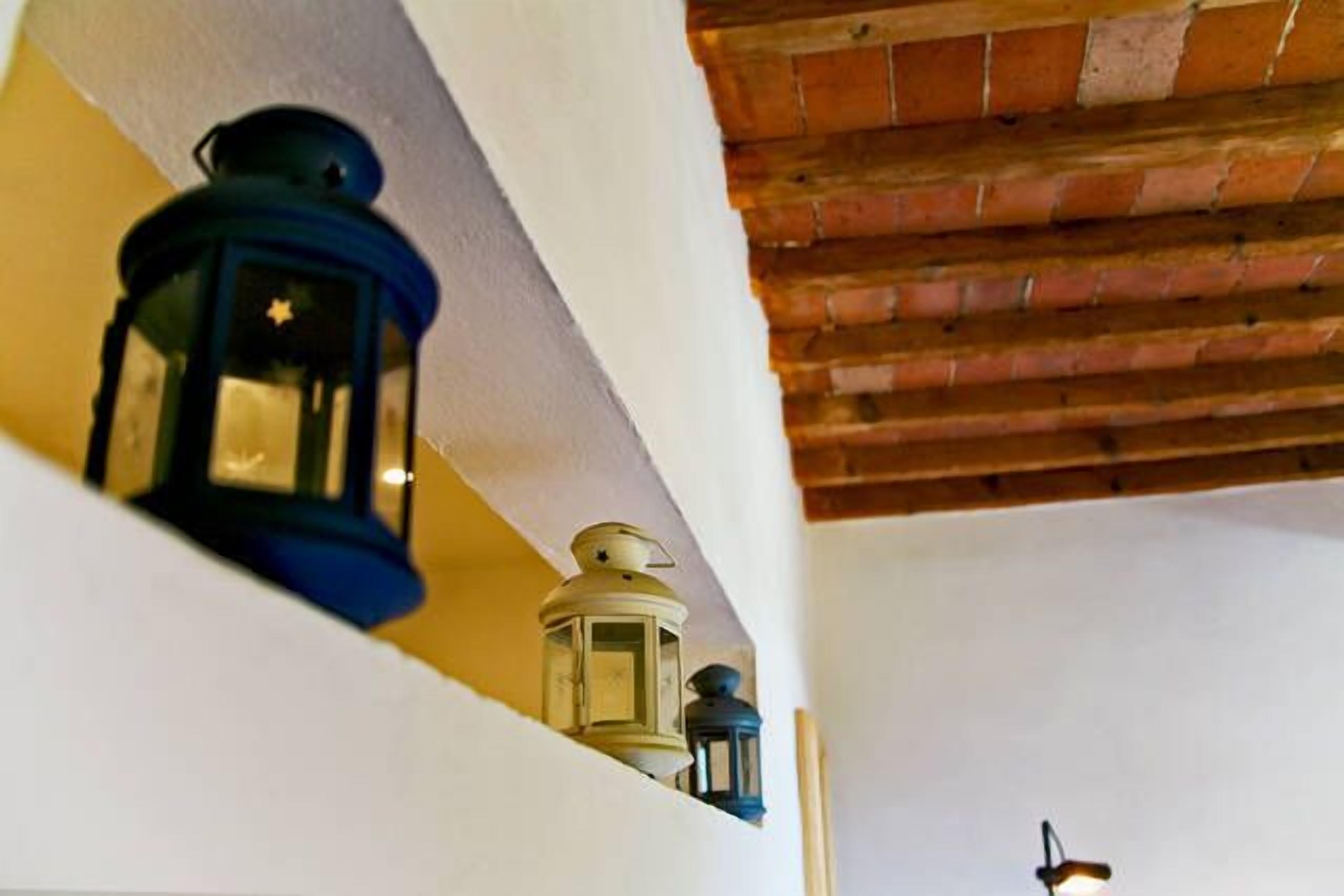 Un coin de pièce avec un mur blanc et un plafond en briques. On peut voir trois lanternes posées sur une étagère.