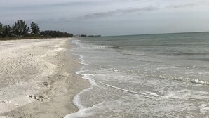 A beach with gentle waves, a sandy shore, and a line of trees in the background. - Breathtaking Beach Front Property Ground Floor Condo (Longboat Key)