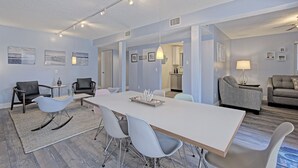 A spacious living room with a large white table, several chairs, and a sofa. There are framed pictures on the walls and a lamp on a side table. - Breathtaking Beach Front Property Ground Floor Condo (Longboat Key)