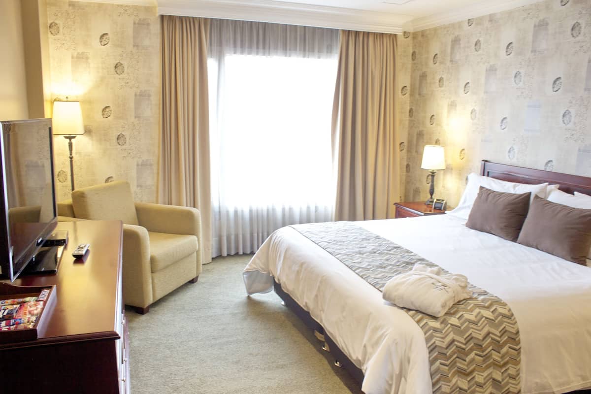 Habitación de hotel con una cama grande, televisor, escritorio con lámpara y una silla.