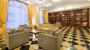Een ontvangsthal met een geruit vloerkleed, banken, een tafel en een boekenkast.