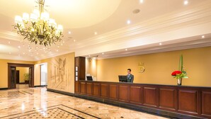 Een hotel receptie met een marmeren vloer, een kroonluchter, een receptiebalie en een bord aan de muur.
