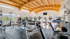 Een fitnessruimte met diverse fitnessapparaten, een houten plafond en grote ramen.