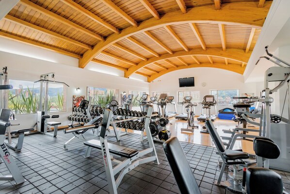 A gym with various exercise equipment, a wooden ceiling, and large windows. - Apartamentos Dann (Bogotá)