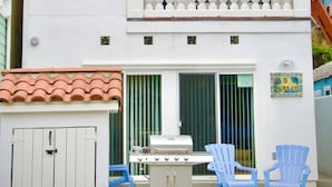Una casa de dos pisos con un balcón, una parrilla y sillas azules en el jardín delantero.