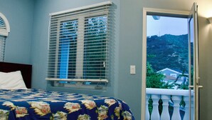 Un dormitorio con cama, ventilador de techo, ventana con persianas y puerta que da a un balcón.