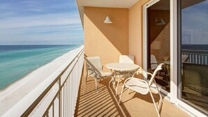 Un balcón con mesa y sillas blancas, con vista a una playa y el océano.