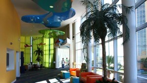 Un hall amplio con techo alto, ventanas grandes y una palmera en el centro.