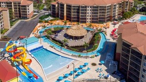 A resort with a central pool, a water slide, and multiple lounge areas with umbrellas.