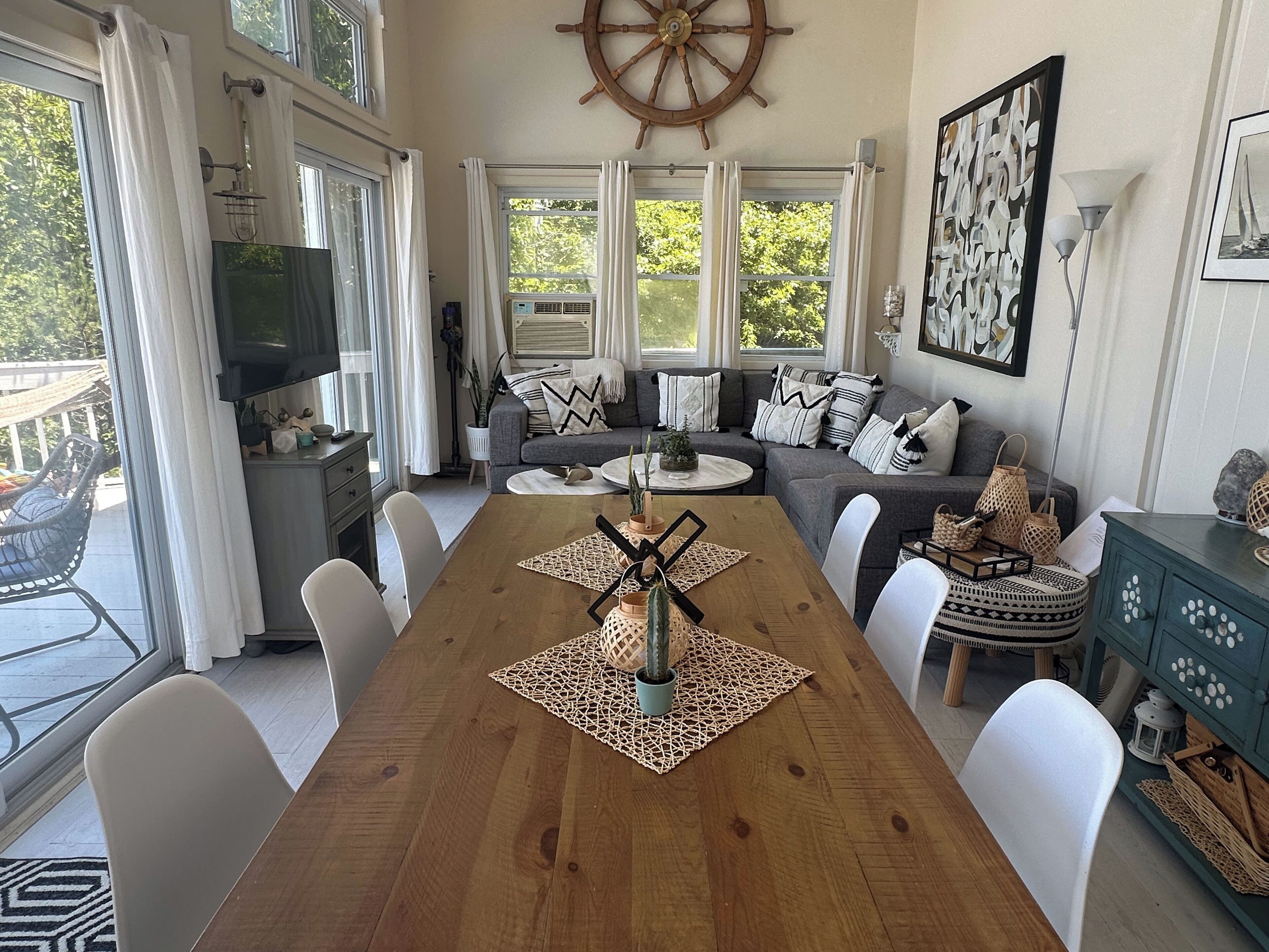 Un salon spacieux avec une table à manger en bois, des chaises blanches, un canapé gris et une grande fenêtre avec des rideaux.