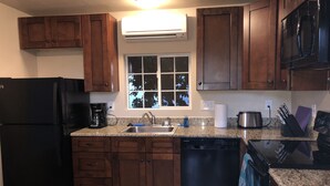 A kitchen with wooden cabinets, a black refrigerator, a dishwasher, a sink, and a window with a view of trees. - Clean, renovated 1 Bedroom with everything you need. Granite, Travertine! (Tucson)