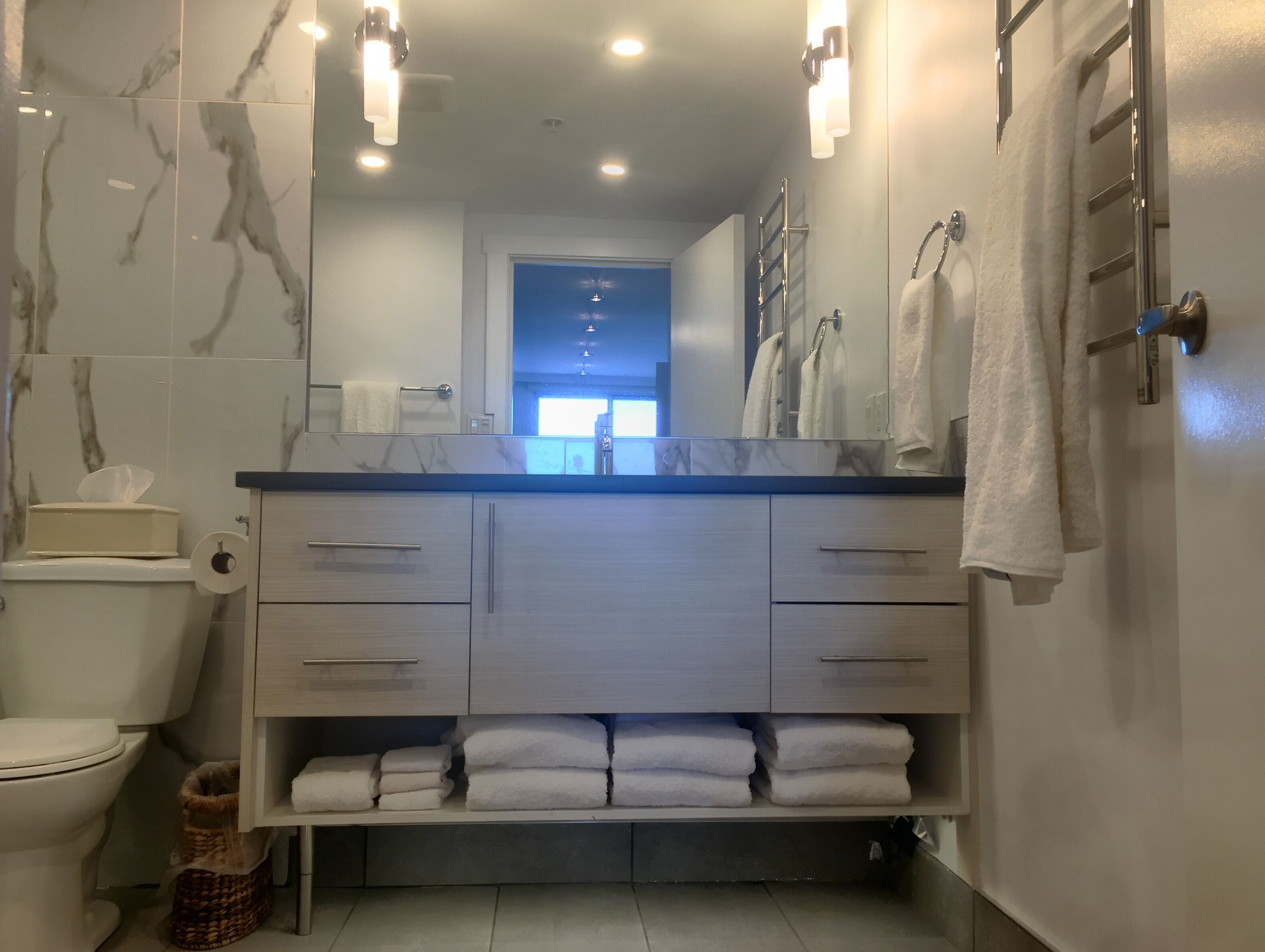 A modern bathroom with a marble backsplash, a large mirror, and a vanity with multiple drawers and a towel rack.