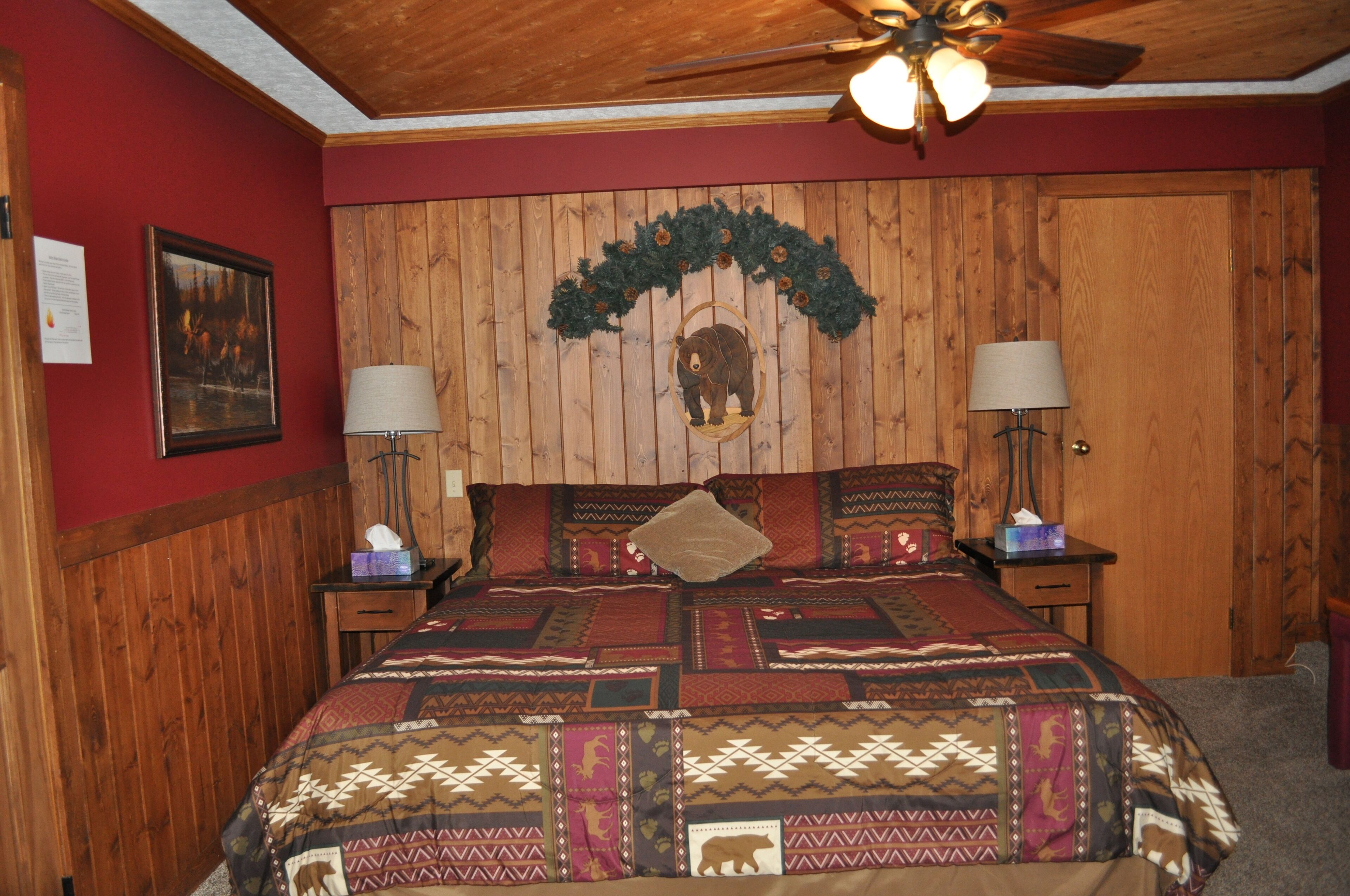 A bedroom with a wooden paneled headboard, a quilted bedspread, two bedside lamps, and a ceiling fan.