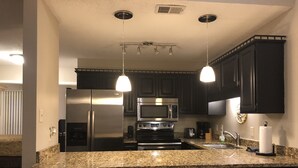 Una cucina moderna con mobili scuri, elettrodomestici in acciaio inossidabile, piani di lavoro in granito e illuminazione a sospensione.
