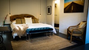 A bedroom with a large bed, a wooden headboard, a bench, a chair, a painting, and a framed picture on the wall. - Chic Apartment-Style Suite, Steps From Main, Luxury Finishings, Outdoor Shower (Fredericksburg)