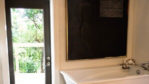 A bathroom with a bathtub, a door leading outside, and a wall-mounted artwork. - Chic Apartment-Style Suite, Steps From Main, Luxury Finishings, Outdoor Shower (Fredericksburg)