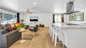 Uma sala de estar moderna com um sofá cinza, uma mesa de centro e uma área de jantar com banquetas brancas.