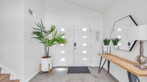 Um corredor moderno com porta branca, um banco de madeira, uma planta em vaso e um espelho na parede.
