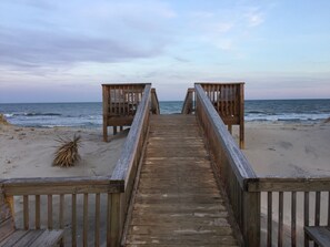 A wooden boardwalk leading to beach chairs on a sandy beach with the ocean in the background.