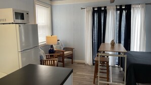 Ein kleiner Raum mit einer Küchenzeile, einem Essbereich mit Tisch und Stühlen, einem Bett und einem Deckenventilator.