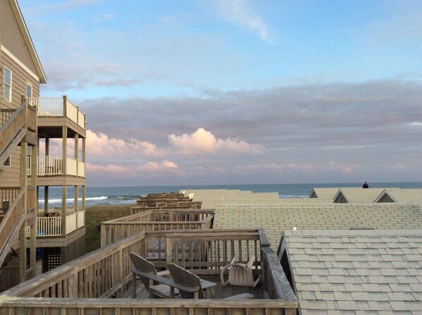 A wooden deck with chairs and a wooden structure with railings overlooking a beach.