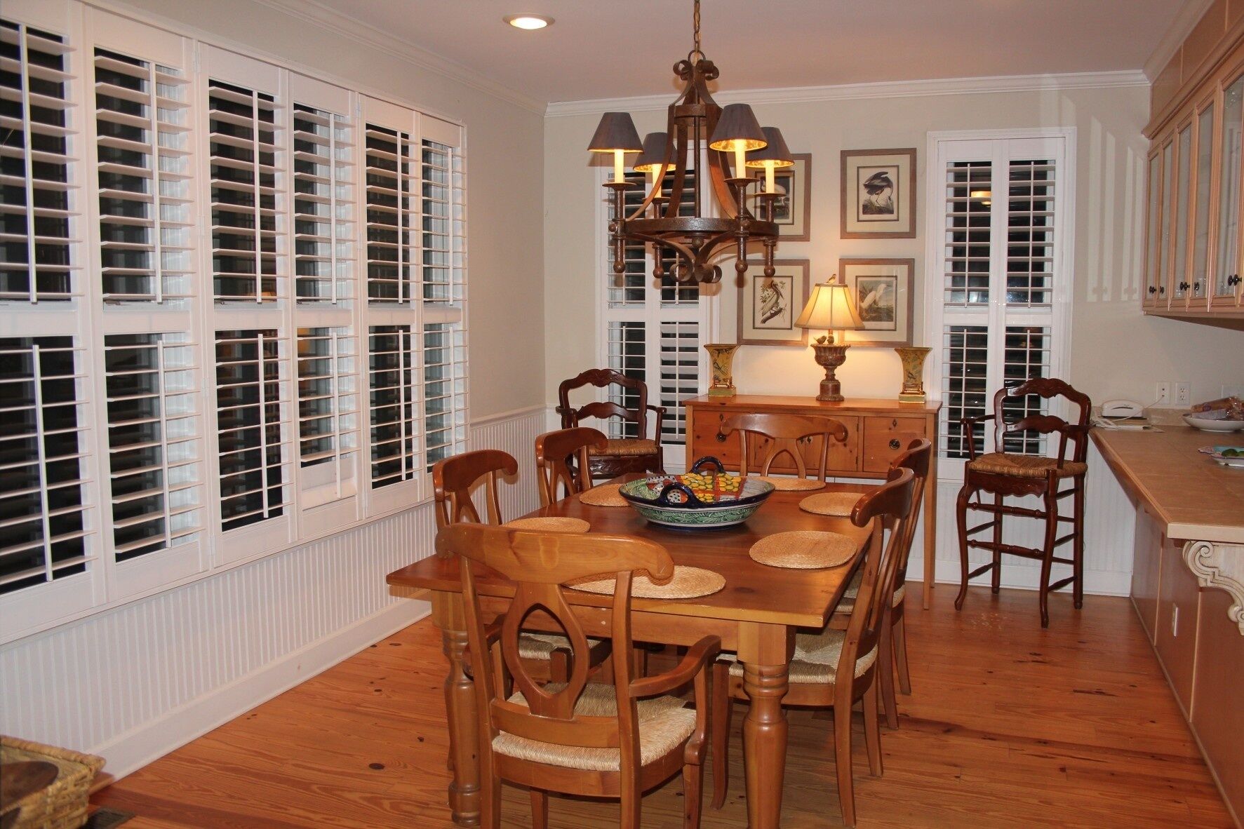 A dining room with a wooden table and chairs, a chandelier, and a window with shutters.