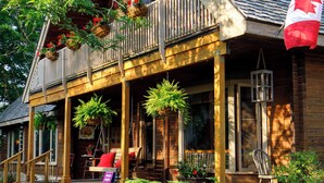 A wooden cabin with a porch, potted plants, and a Canadian flag. - Runaway Rooster B&B - The Coop (Prince Edward)
