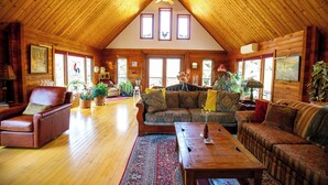 A spacious log cabin interior with a high ceiling, wooden walls, and a large living area furnished with sofas, a coffee table, and potted plants. - Runaway Rooster B&B - The Coop (Prince Edward)