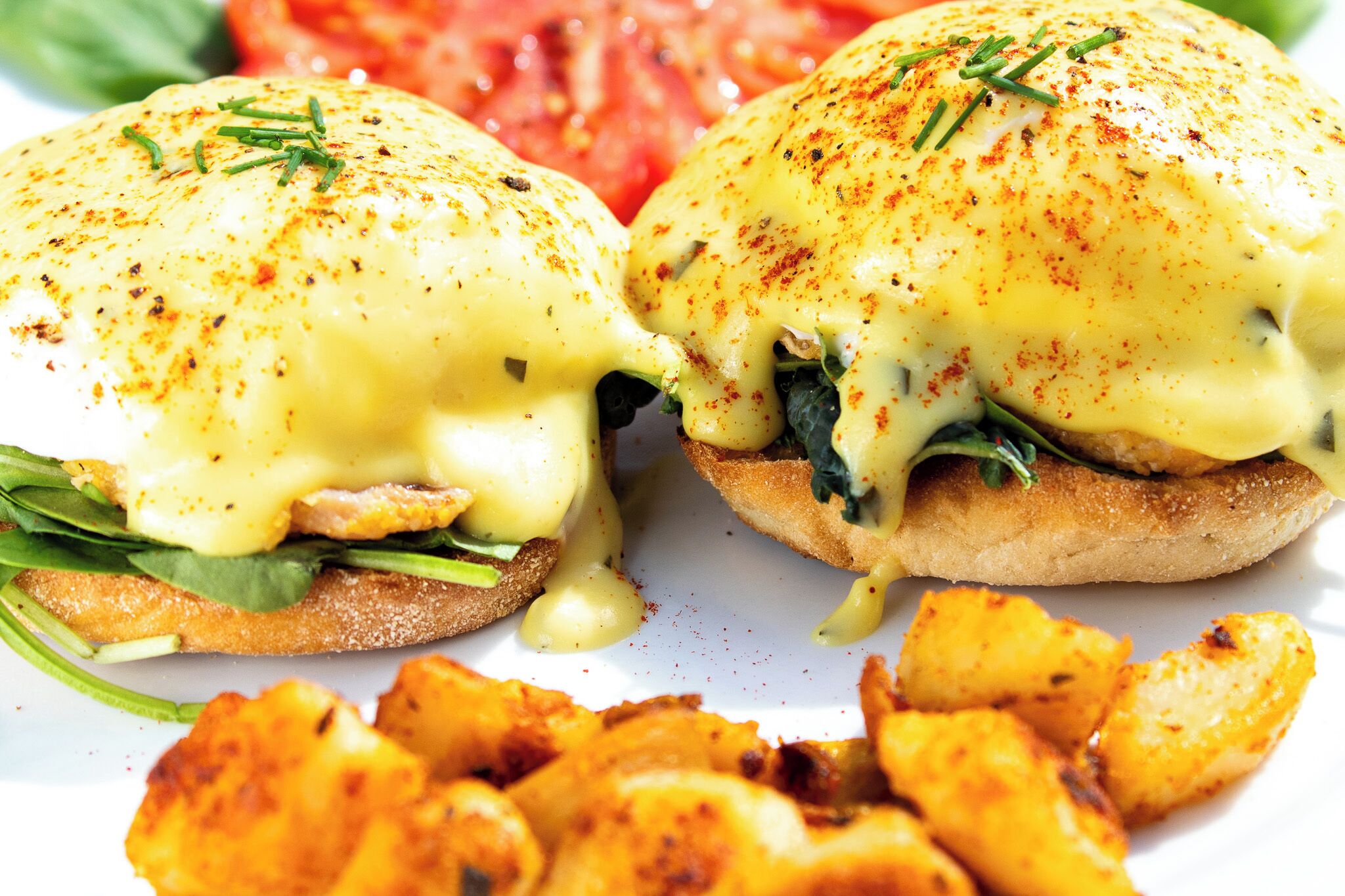 A breakfast plate with eggs benedict, spinach, and potato wedges.