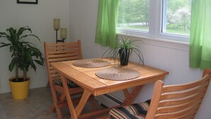 A wooden dining table with two woven placemats, a potted plant, and a chair with a striped cushion. - Apt. retreat near lake and 215' waterfall, peaceful, lovely gardens.  (Trumansburg)