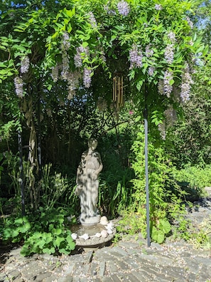 Un jardín con una estatua, abundante vegetación y una fuente de piedra.
