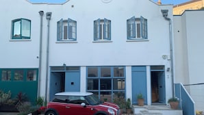 A red Mini Cooper parked in front of a white building with blue shutters and a blue door.