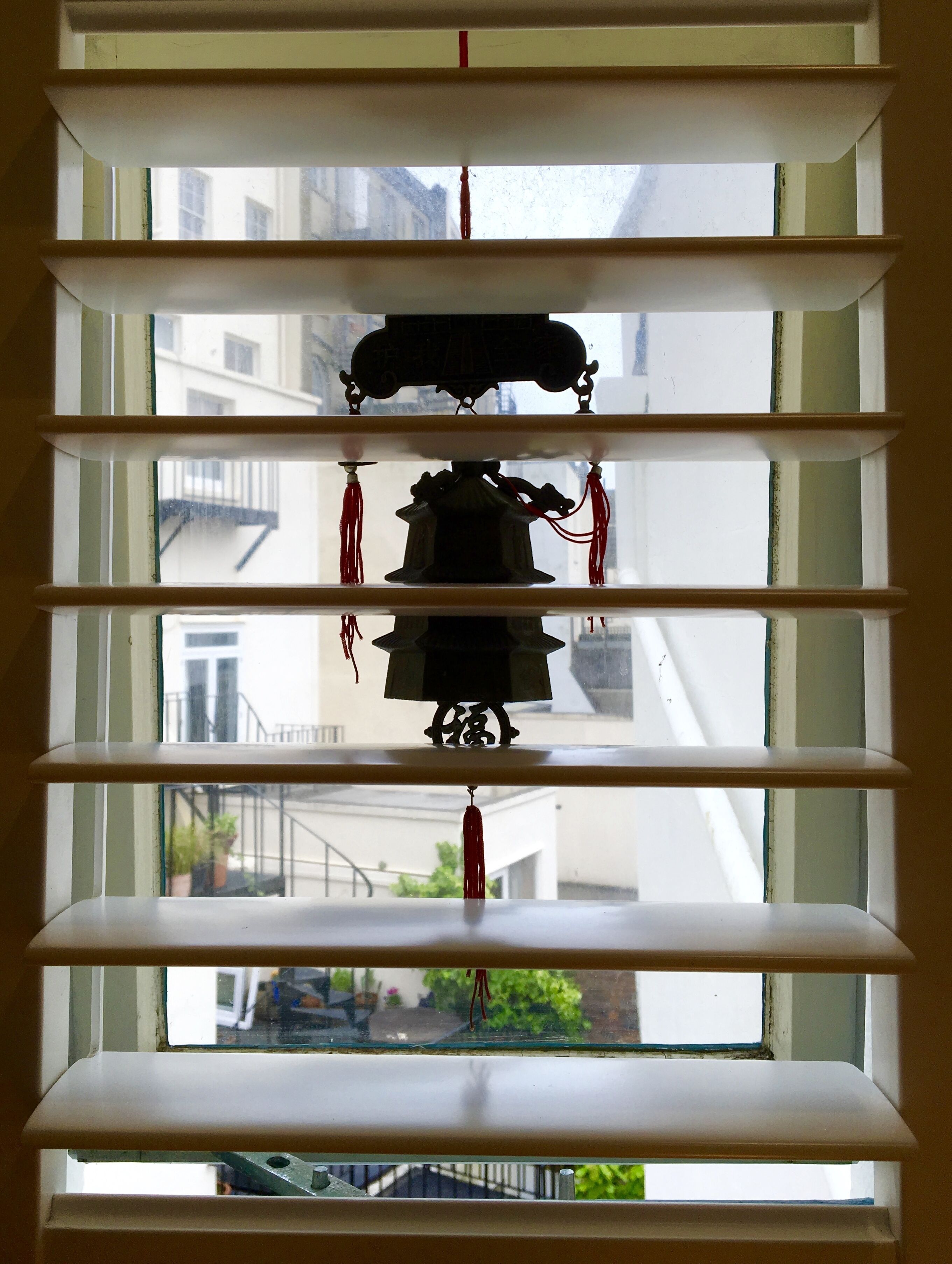 Una ventana con persianas horizontales y una campana decorativa colgando en el centro.