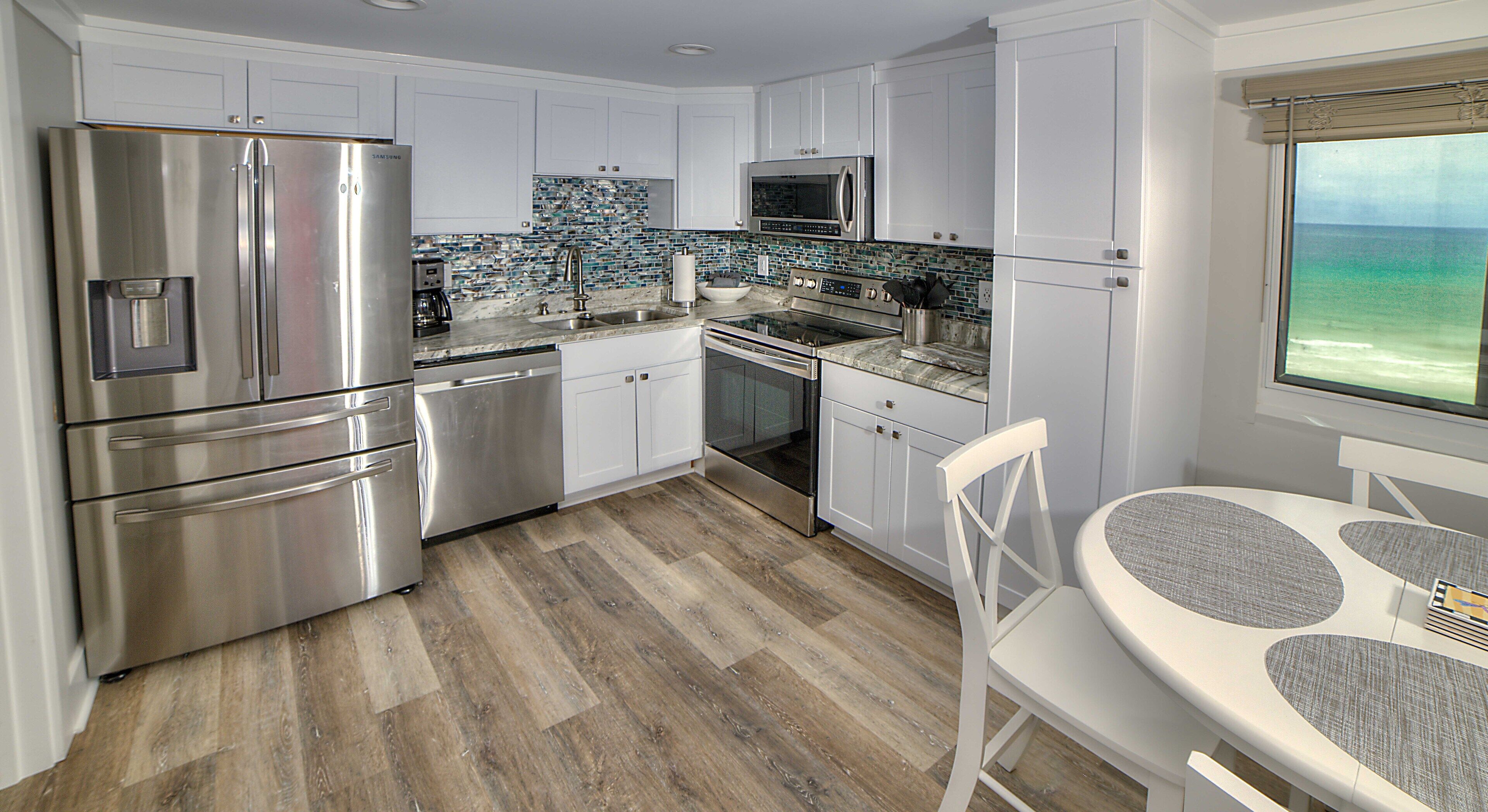 A modern kitchen with stainless steel appliances, white cabinetry, and a wooden floor.