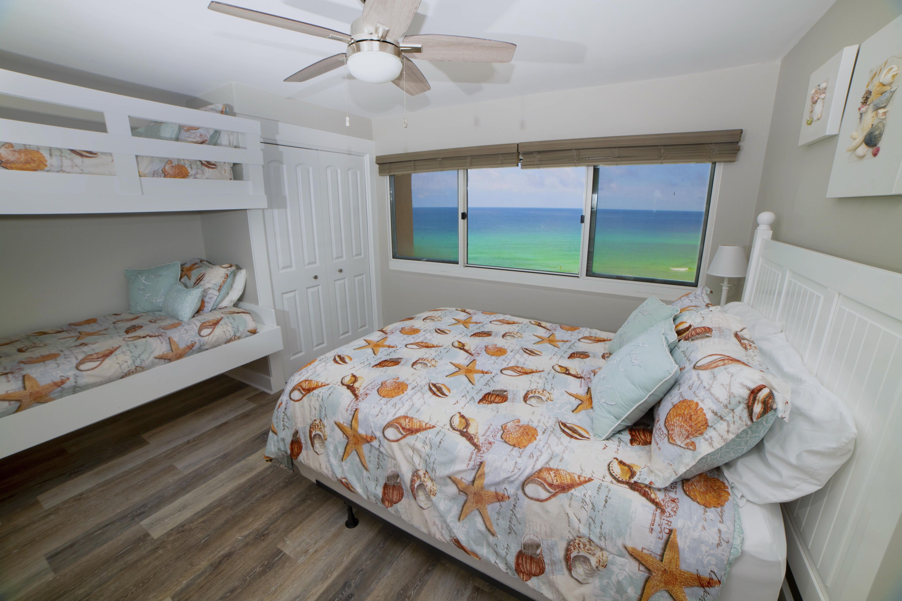 A bedroom with a view of the ocean, bunk beds, and a ceiling fan.