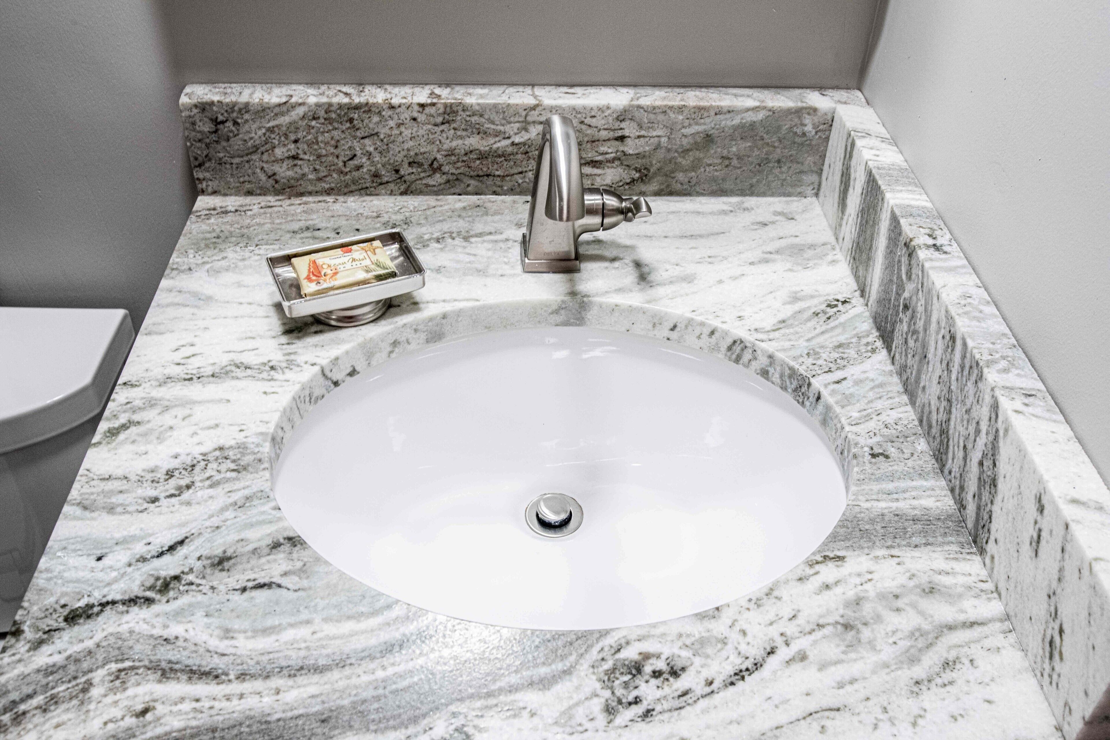 A bathroom with a marble sink, a modern faucet, and a small tray with a toothbrush.