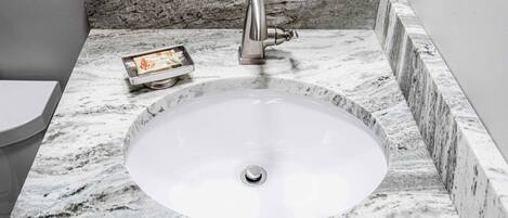 A bathroom with a marble sink, a modern faucet, and a small tray with a toothbrush.