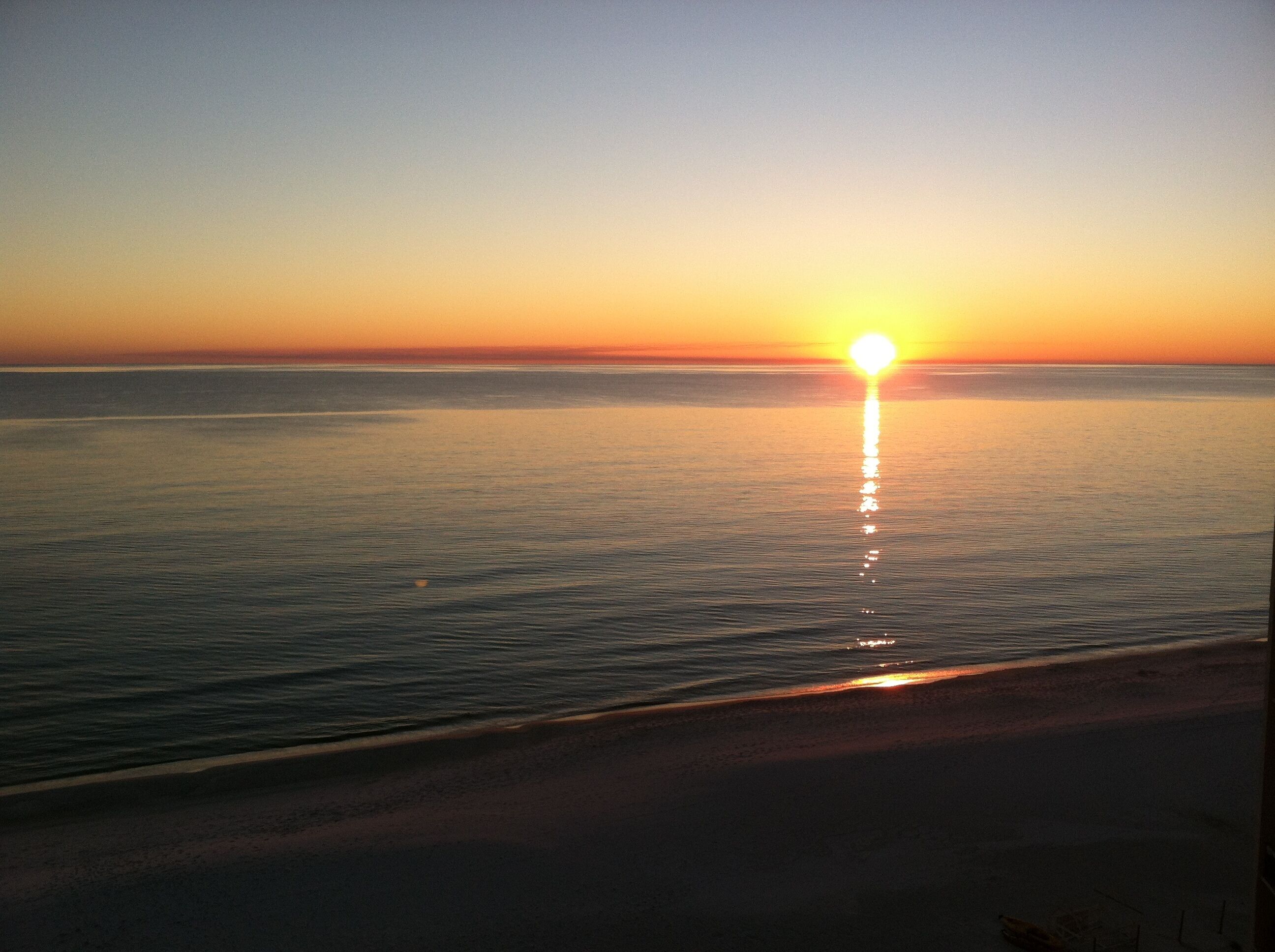 A sunset over a calm sea with a beach in the foreground.