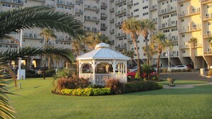 Un hotel de varios pisos con un patio central que cuenta con un pabellón, palmeras y césped cuidado.