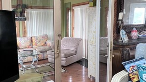 A spacious living area with a high ceiling, wooden flooring, a large window, and a cozy seating arrangement.