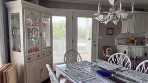 A dining area with a glass-top table, white chairs, and a white cabinet with glass doors.