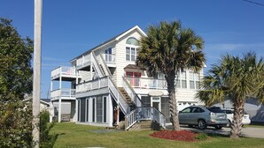 A multi-story house with a balcony, a staircase, and a palm tree in the yard.