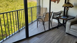 A balcony with a view of greenery and a body of water. There is a table with a lamp and chairs. - Luxury Condominium In Key Largo... Sunsets, Marina (Key Largo)