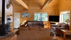 A cozy cabin interior with a wooden ceiling, a fireplace, a sofa, and a television. - Riverfront Paradise - Minutes from Wolf Creek Ski Area (South Fork)