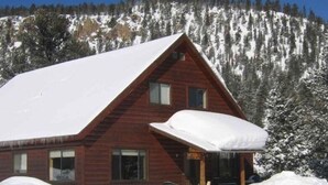 A wooden cabin with a snow-covered roof and a small porch. - Riverfront Paradise - Minutes from Wolf Creek Ski Area (South Fork)