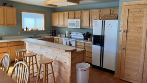 A kitchen with wooden cabinets, a white refrigerator, a microwave, and a wooden island with stools. - Riverfront Paradise - Minutes from Wolf Creek Ski Area (South Fork)