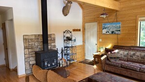 A cozy living room with a stone fireplace, wooden furniture, and a hanging light fixture. - Riverfront Paradise - Minutes from Wolf Creek Ski Area (South Fork)
