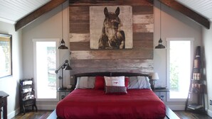 Une chambre avec un grand lit, un mur en bois et un tableau représentant un cheval.